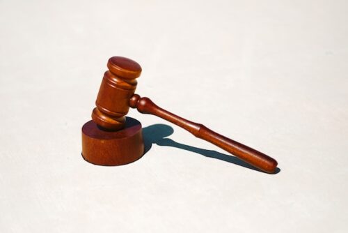 A wooden judge's gavel, used for federal laws, resting on a white surface, casting a sharp shadow.